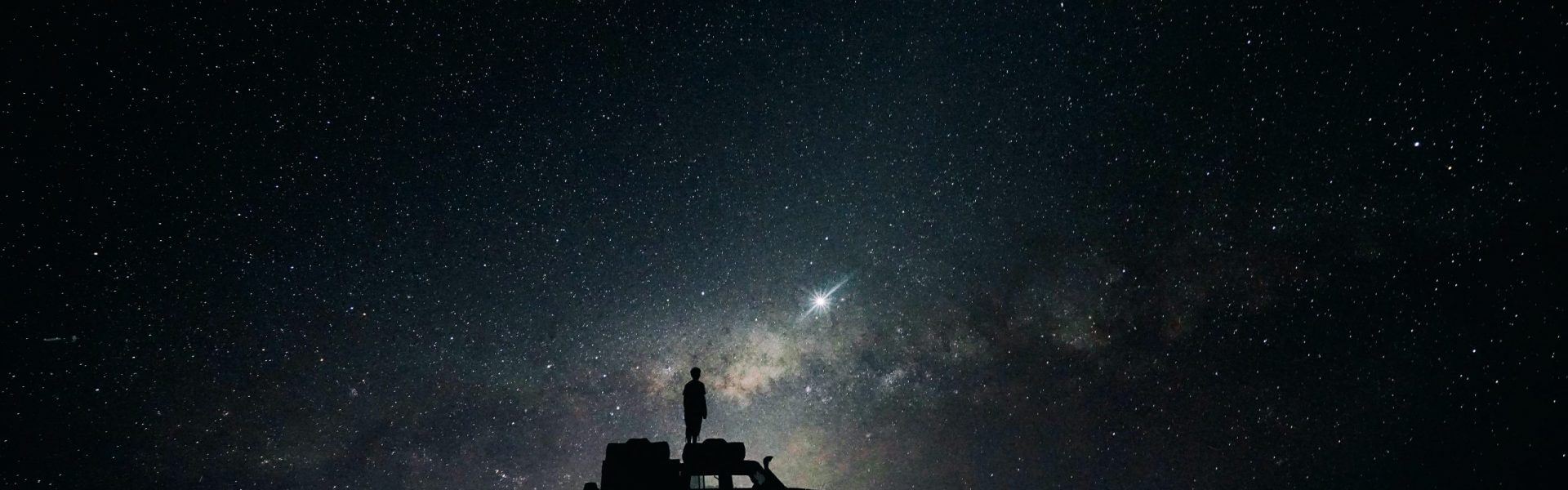 Silhouette of man standing on car in front of night sky